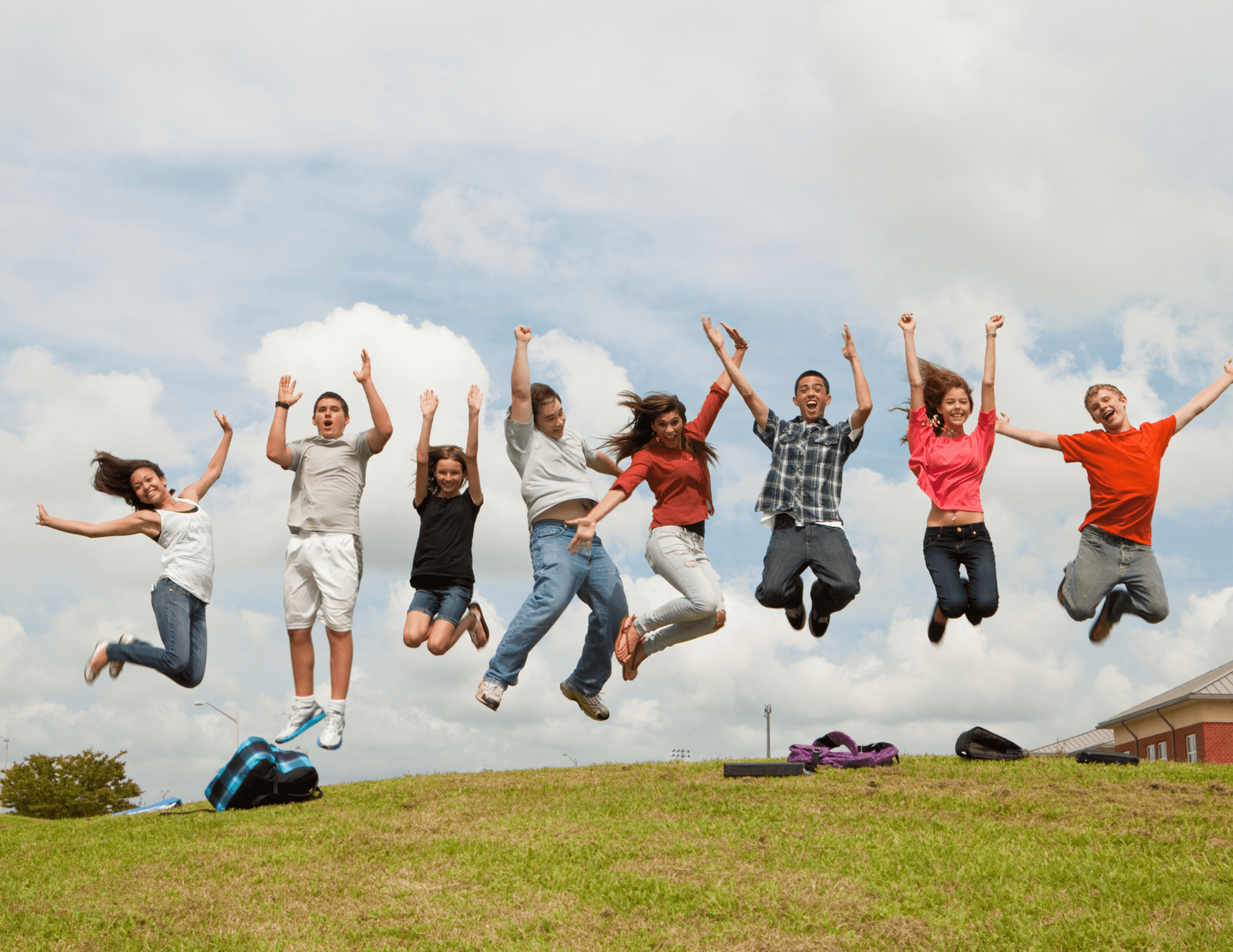 A lively group of eight young teenagers, leaping simultaneously in the air, arms to the sky, in a moment of shared joy.