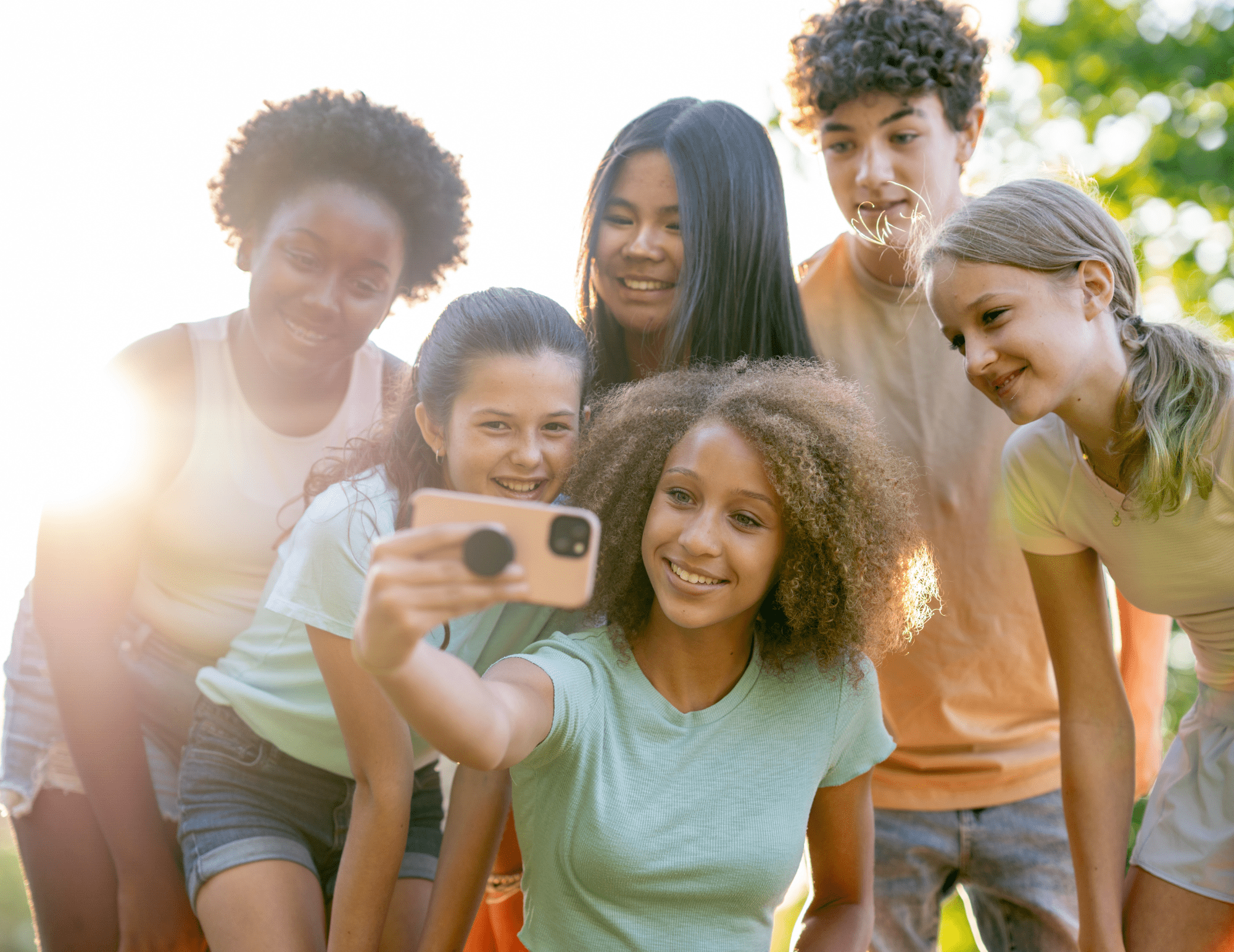 Six cheerful preteens from different backgrounds taking a selfie outside on a warm summer day.