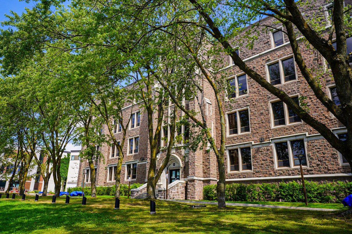 Stone building at Cégep de Saint-Jérôme with large windows and trees lining a grassy lawn.