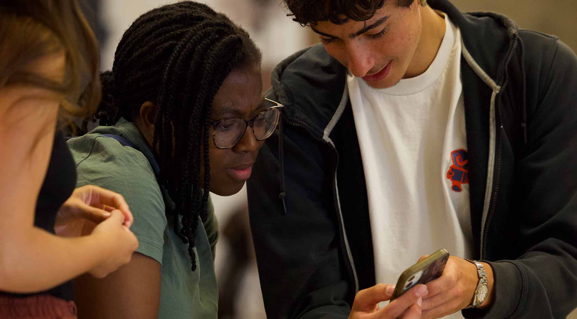 1 – HomePage_Image6 – FINAL Student standing on a bus with his headphones and backpack on, holding a phone and focusing on the screen.
